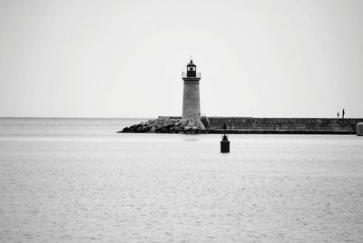 Lighthouse by sea against clear sky