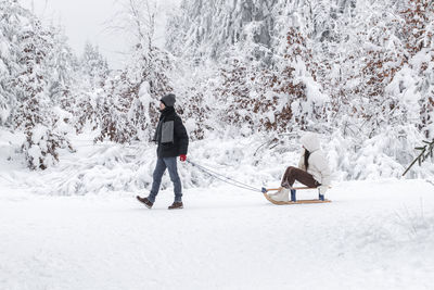 A young guy rides a girl on a sleigh in the forest.