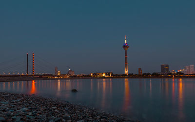 Illuminated buildings by river against sky at night