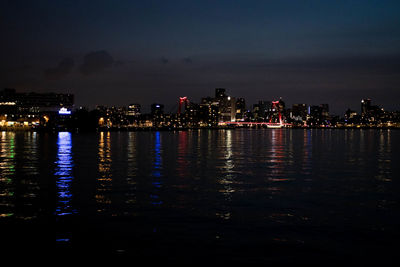 Illuminated buildings by sea against sky at night