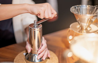 Female hand mash coffee bean in coffee grinder on wooden table.