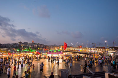 Crowd in illuminated city against sky at dusk