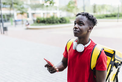 Confused delivery man wearing wireless headphones holding mobile phone