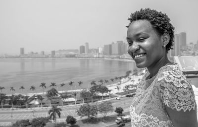 Portrait of smiling young woman in city against clear sky