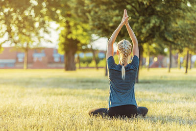 Rear view of woman exercising yoga on grassy field at park