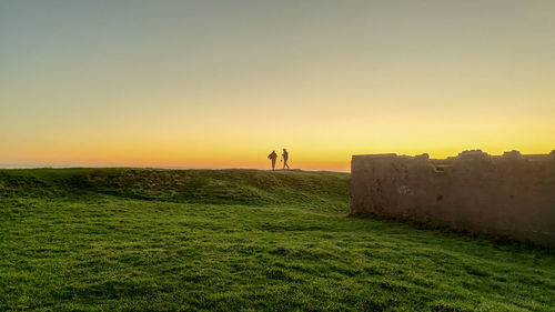 People standing on field against sky during sunset