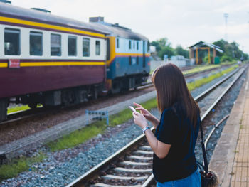 Woman using mobile phone while standing at railroad track