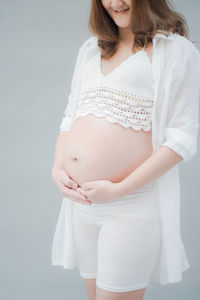 Midsection of smiling pregnant woman standing against gray background