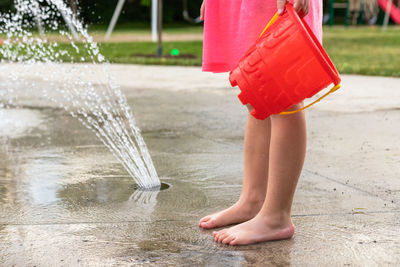 Little child playing barefoot with water and toys at splash pad in public park playground in summer