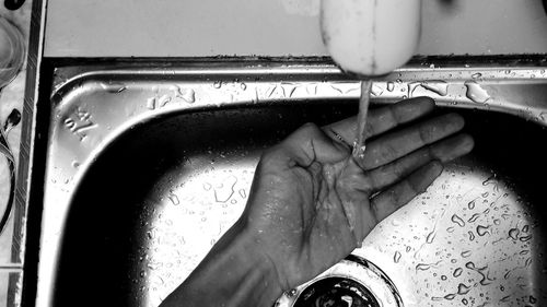 Close-up of hand touching water from faucet at home