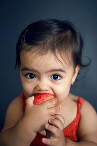 Baby girl in red tank top eating ripe red apple on black background in studio