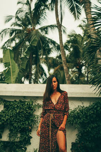 Young woman standing by palm tree against plants