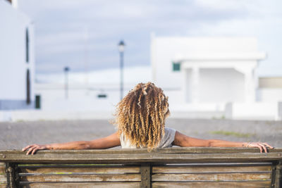 Rear view of woman with curly hair sitting on bench