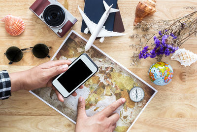 Cropped hands of man holding mobile phone over map at table