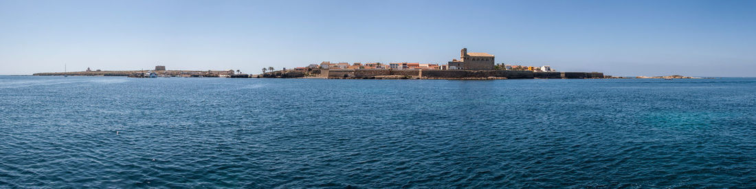 Sea by buildings against clear blue sky