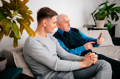 Father and son using phone sitting on sofa