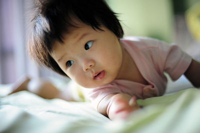 Close-up of cute baby girl lying down on bed