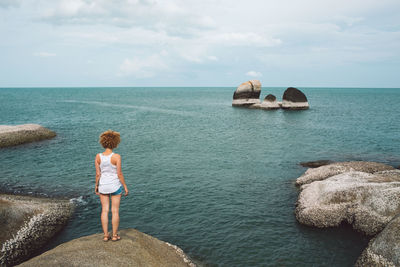 Rear view of woman standing by sea on rock