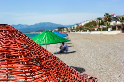 Close-up of orange wicker parasol at beach against sky