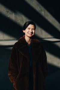 Portrait of happy young woman standing against wall