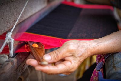 Cropped hand of woman holding needle by handloom at workshop