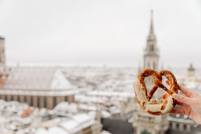 Close-up of hand holding pretzel against buildings in city munich