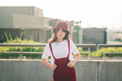 Portrait of woman standing against railing in city