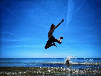 Boy jumping in sea against blue sky