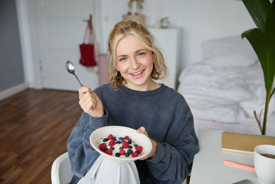Portrait of smiling young woman eating food at home