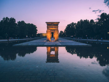 Reflection of built structure in water against sky at sunset