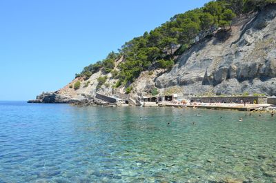 Scenic view of sea by mountains against clear blue sky