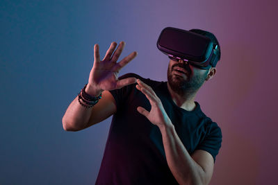 Young man in vr glasses excited interact with virtual reality in color neon light, future technology