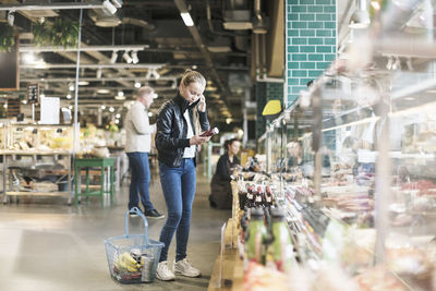 Girl using smart phone while reading label on bottle in organic groceries store