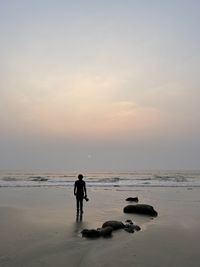Man standing on beach against sky during sunset