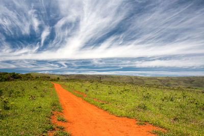 Dirt road amidst field against sky