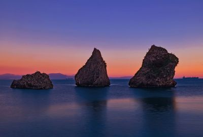 Rocks in sea against sky during sunset