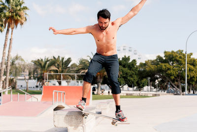 Full length of shirtless man skateboarding at skate park
