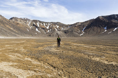 Rear view of man walking on mountain against sky