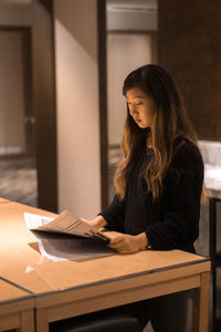 Young woman reading newspaper on table at home