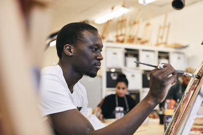 Side view of young male student painting on artist's canvas in art class