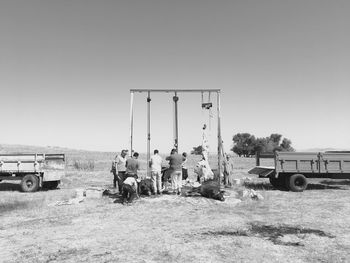 Group of people relaxing on field against clear sky