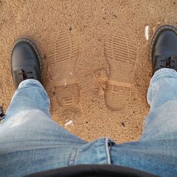 Low section of man standing by shoe prints at beach