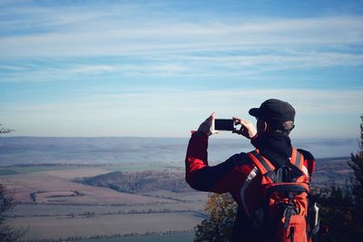 Rear view of man photographing landscape against sky