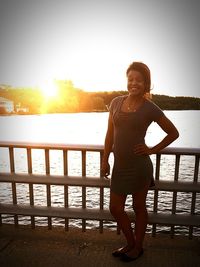 Portrait of smiling young woman standing against sea at sunset