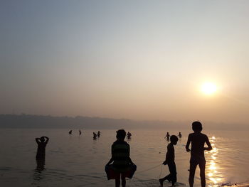 Silhouette people standing on beach against sky during sunset