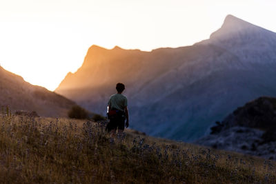 Back view of unrecognizable traveler standing in grassy valley and admiring mountain ridge at sunrise in pyrenees