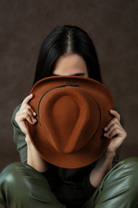 Young woman with black hair hides her face behind a hat