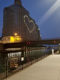 Illuminated bridge over river by buildings against sky in city