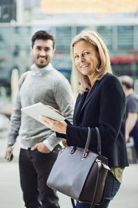 Portrait of businesswoman using digital tablet on city street with colleague in background