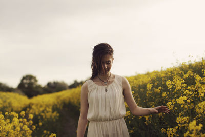 Young woman standing on field against sky